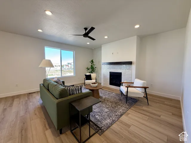 Living area featuring wood-finish flooring, recessed lighting, ceiling fan, and a fireplace with a textured tile surround and a dark wood mantel