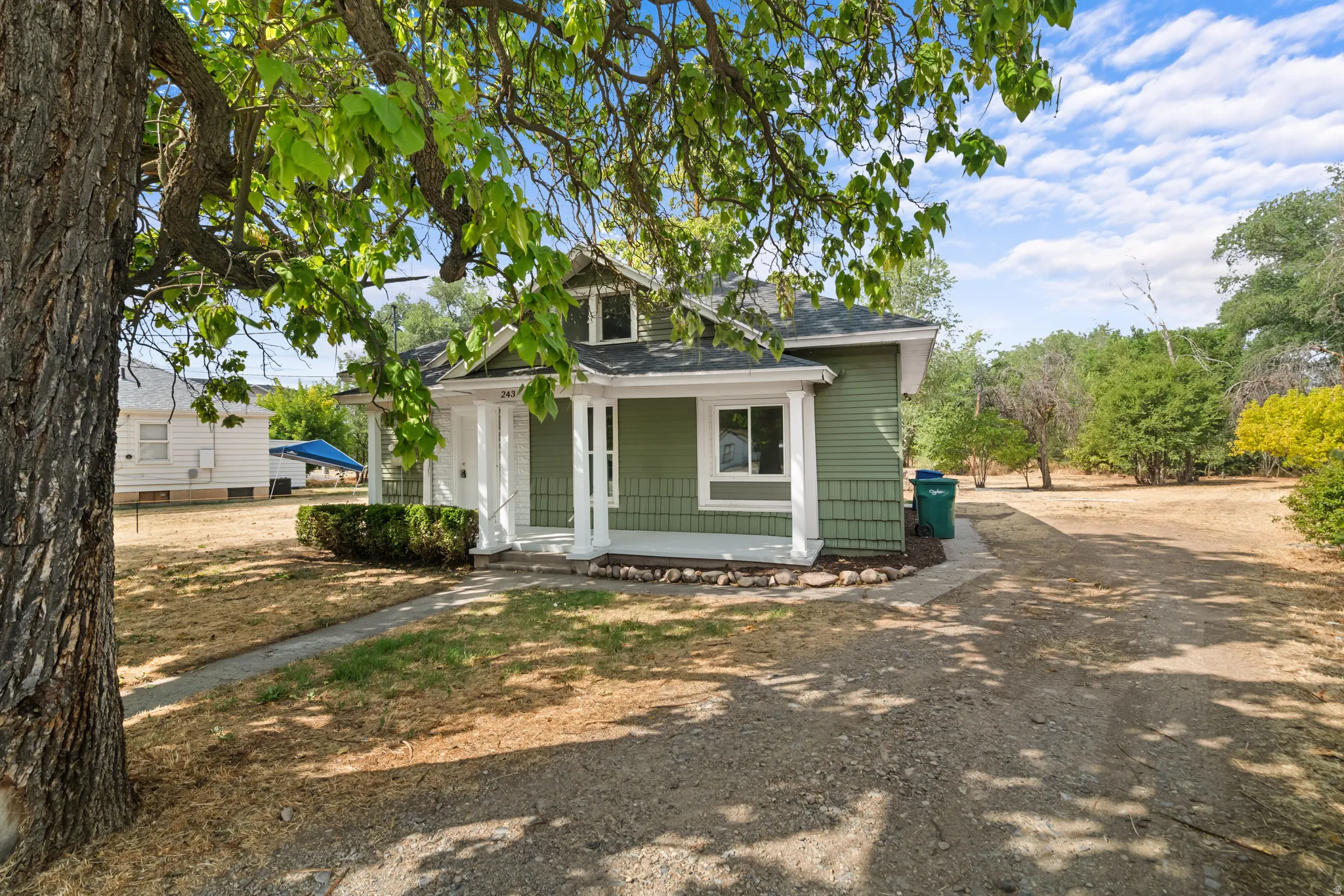 Green siding exterior with a covered porch, white columns, and a dormer window