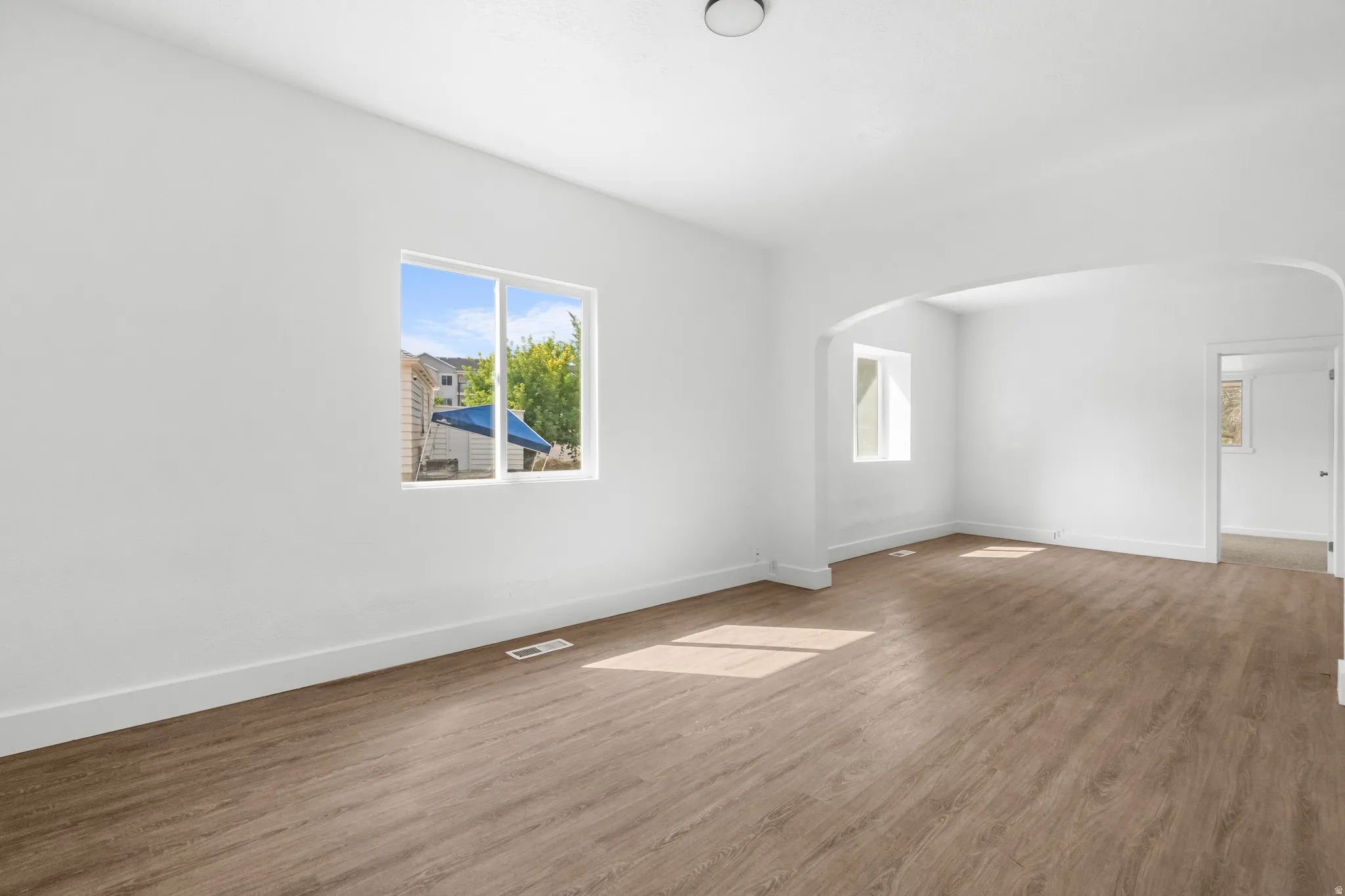 Spacious room featuring wood-finish flooring, white walls, and an arched entryway