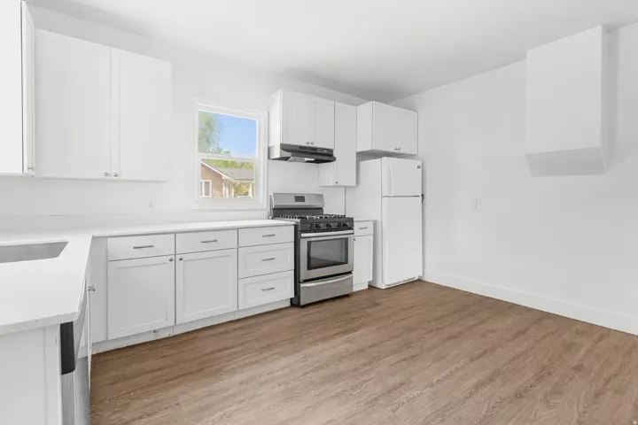 White shaker cabinetry with modern silver hardware, complemented by white countertops, stainless steel appliances, and wood-finish flooring