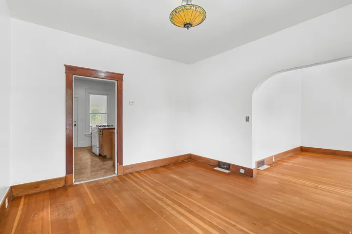 Hardwood flooring, white walls, wood trim, arched doorway, and a decorative ceiling light fixture