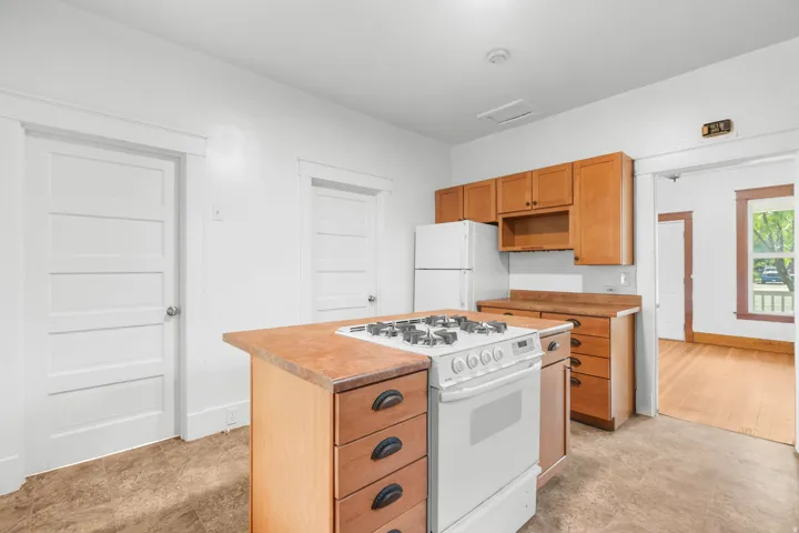 Kitchen featuring wood-finish cabinetry, solid surface countertops, a freestanding gas range, and a refrigerator
