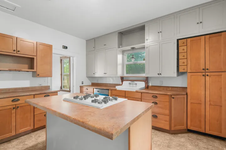 Kitchen featuring mixed wood-finish and painted cabinetry, a central island with a built-in cooktop, and a double basin sink