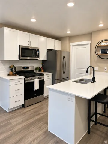White cabinetry with brushed nickel hardware, stainless steel appliances, wood-finish flooring, white countertops, and a white subway tile backsplash