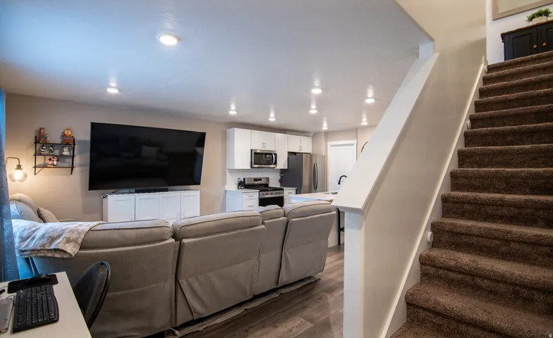 Open concept living area with recessed lighting, wood-finish flooring, and a kitchen featuring white cabinetry and stainless steel appliances