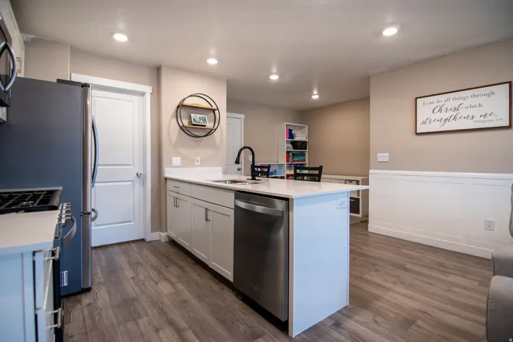 Kitchen island featuring a stainless steel dishwasher, an integrated sink with a matte black faucet, and light-toned cabinetry