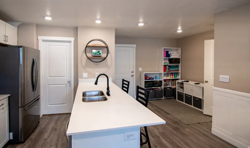 Kitchen featuring a dual-basin sink with a matte black faucet, a large center island with a white countertop, and wood-finish flooring