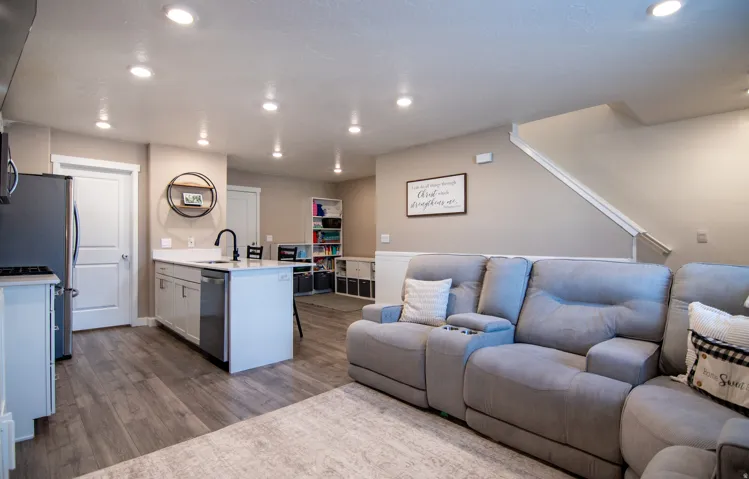 Open-concept living area featuring wood-finish flooring, recessed lighting, a white kitchen island with an undermount sink, and a staircase with white risers and handrails