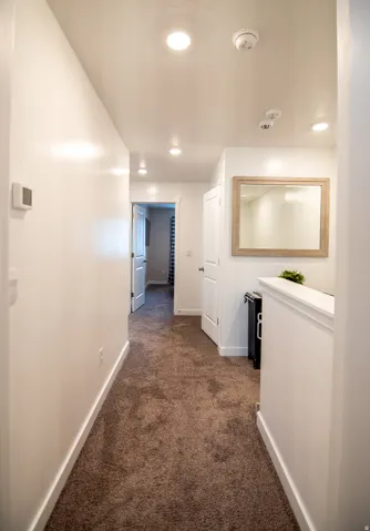 Recessed lighting illuminates the hallway, featuring light-toned walls and brown carpeting