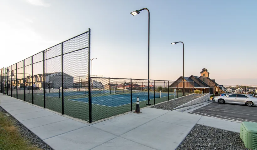 Recreational court area with chain-link fencing, paved walking paths, and integrated lighting