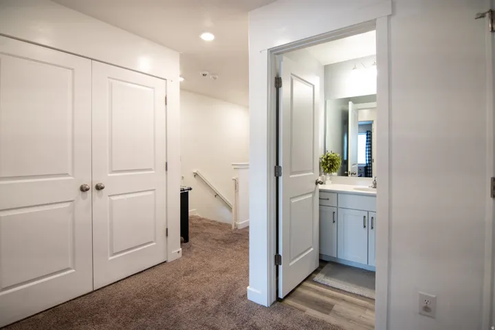 White paneled doors, recessed ceiling lighting, light gray vanity with white countertop, mirrored wall, and wood-finish flooring