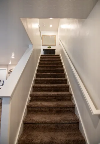 Carpeted staircase with white handrails and recessed lighting