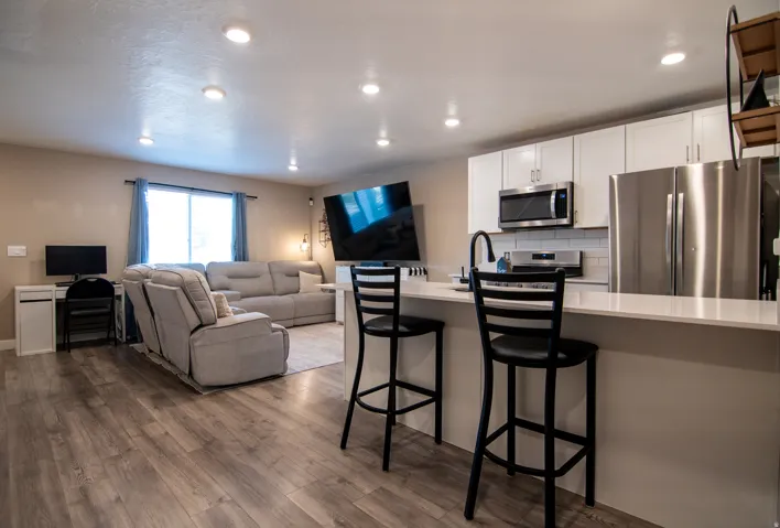 Wood-finish flooring throughout, recessed lighting, white kitchen cabinetry with stainless steel appliances, and a kitchen island with seating