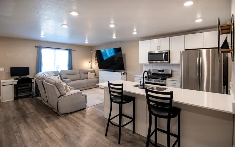 Open-concept living space with wood-finish flooring, recessed lighting, and a white kitchen island with counter seating
