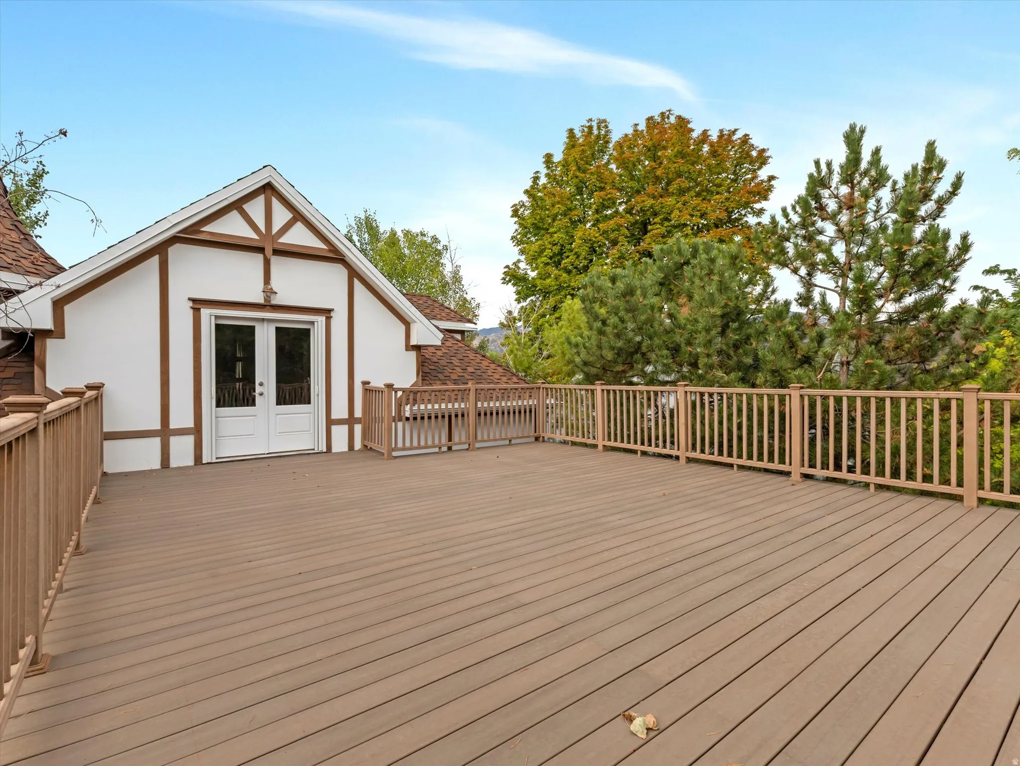 Expansive brand new composite deck featuring horizontal wood-finish railings and a gable-roof structure with decorative timber framing and French doors
