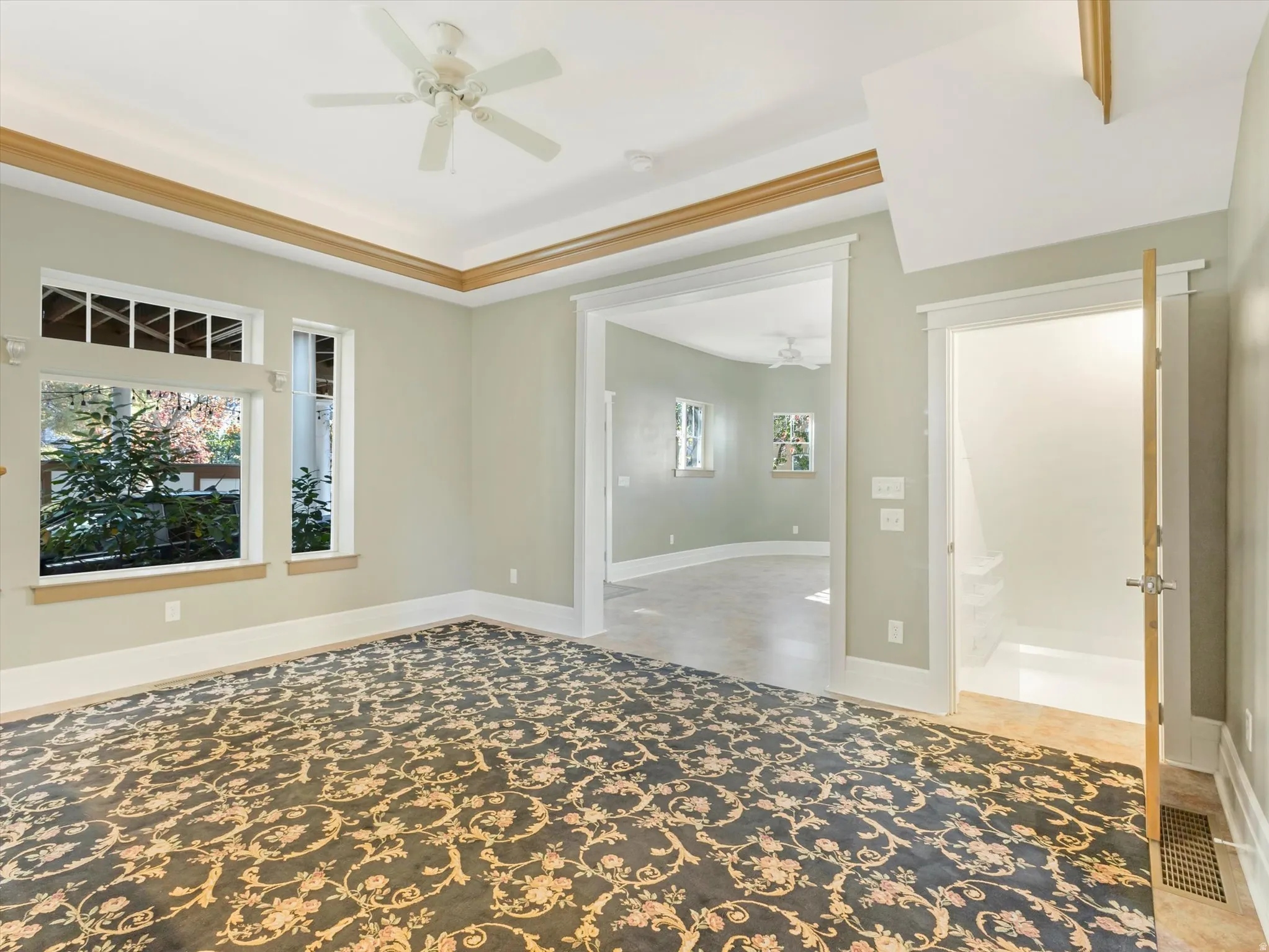 Recessed ceiling with wood trim, ceiling fan, multiple windows, patterned carpet, and an open doorway