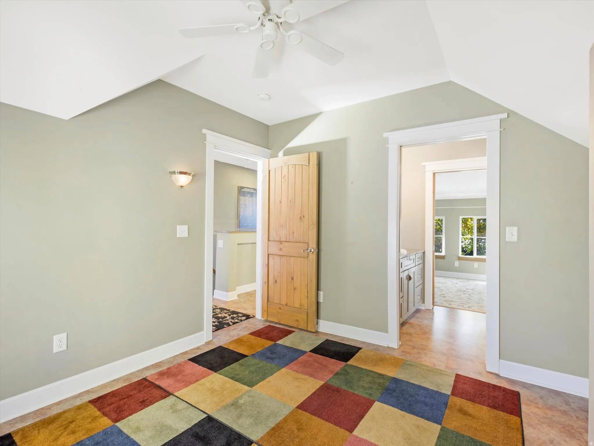 Vaulted ceiling with a ceiling fan, wall sconce lighting, and a wood-finish interior door