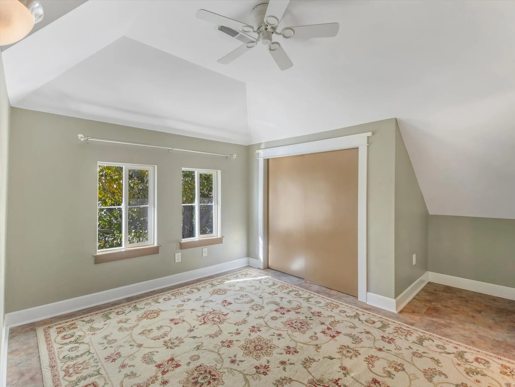 Vaulted ceiling with an attached ceiling fan, dual transom windows, and a built-in closet with sliding doors