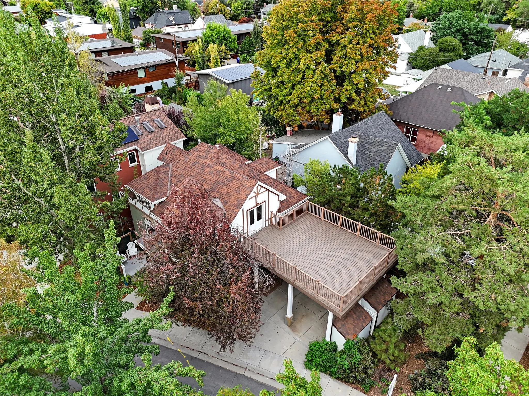 Aerial view showcasing a brick residence with a spacious composite deck, mature landscaping throughout the lot, and established trees providing substantial canopy coverage