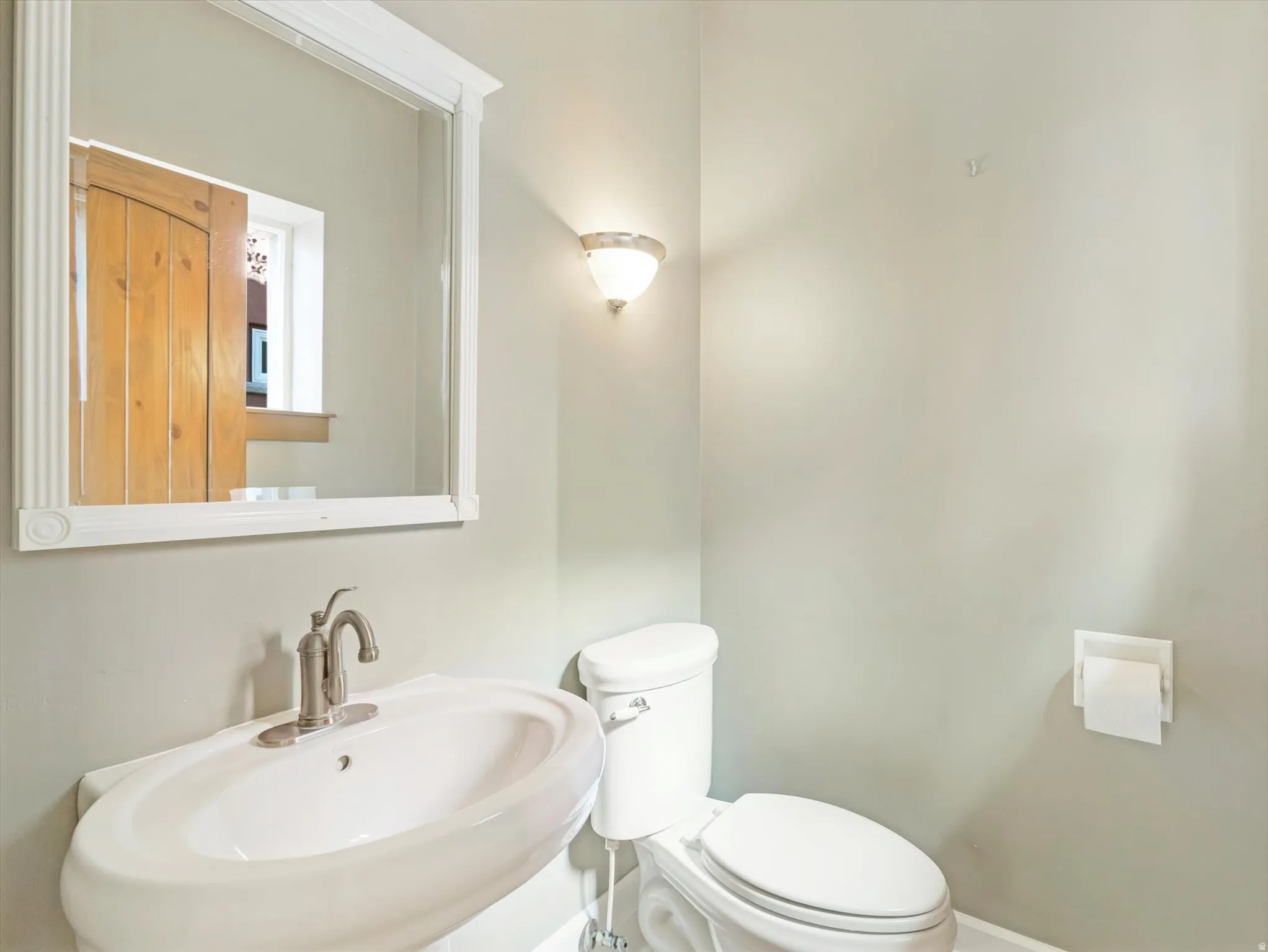 Pedestal sink with a brushed nickel faucet, wall-mounted mirror with decorative frame, and a flush toilet