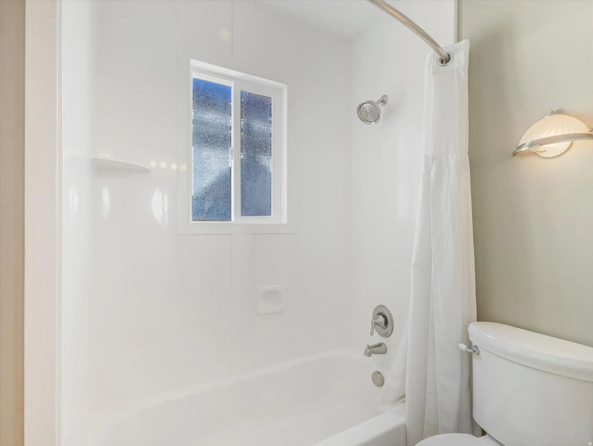 Bathtub with shower, chrome fixtures, integrated shelving, and a privacy window