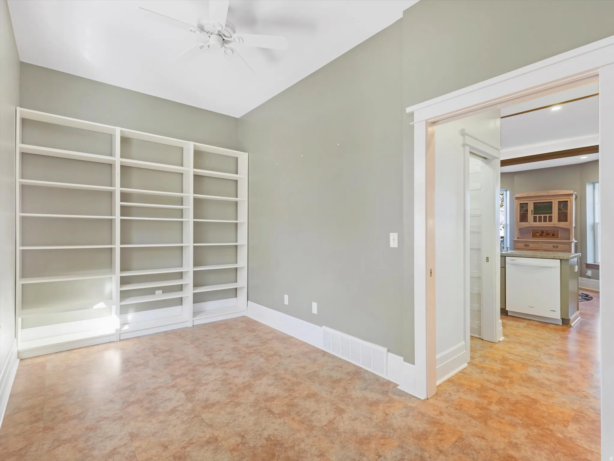 Built-in shelving, ceiling fan, and light-toned flooring