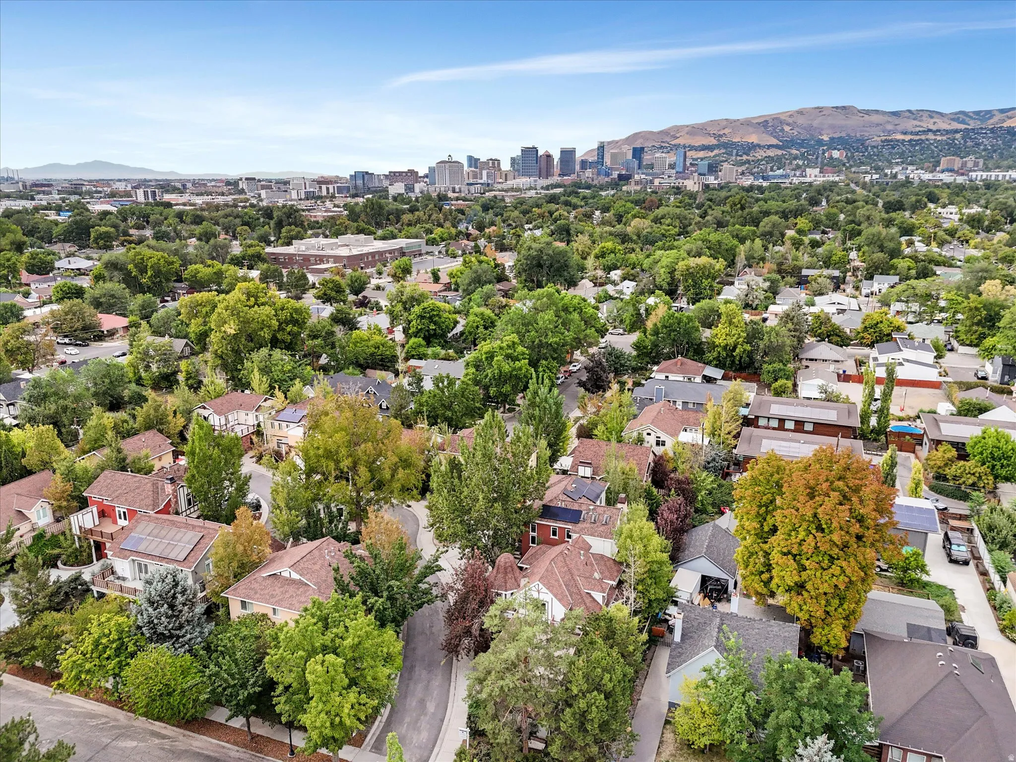 Residential neighborhood with a mountain backdrop, mature trees, and urban skyline in the distance