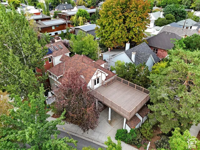 Aerial view showcasing a brick residence with a spacious composite deck, mature landscaping throughout the lot, and established trees providing substantial canopy coverage