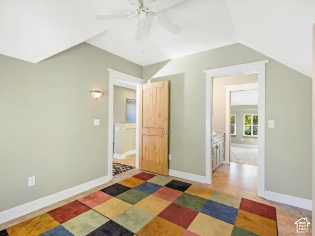 Vaulted ceiling with a ceiling fan, wall sconce lighting, and a wood-finish interior door