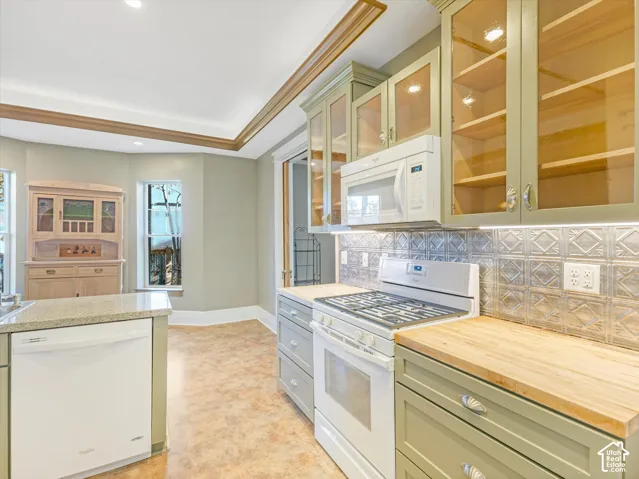 Kitchen featuring light green cabinetry with glass-front upper doors, wood-finish countertops, stainless steel appliances, and a textured metal backsplash