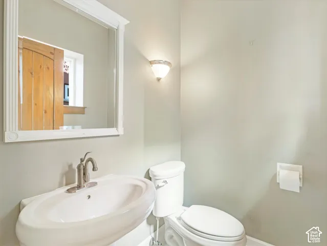 Pedestal sink with a brushed nickel faucet, wall-mounted mirror with decorative frame, and a flush toilet