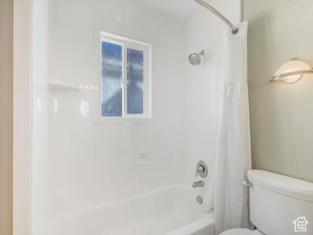 Bathtub with shower, chrome fixtures, integrated shelving, and a privacy window