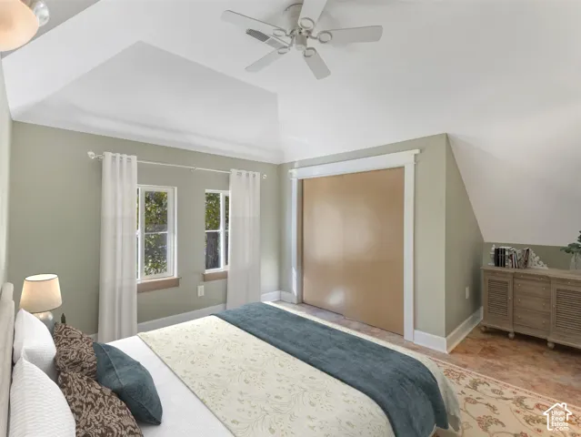 Primary bedroom suite featuring vaulted ceilings with ceiling fan, wood-finish flooring, soft sage green walls with white trim, French doors opening to exterior space, and built-in dresser with shelving