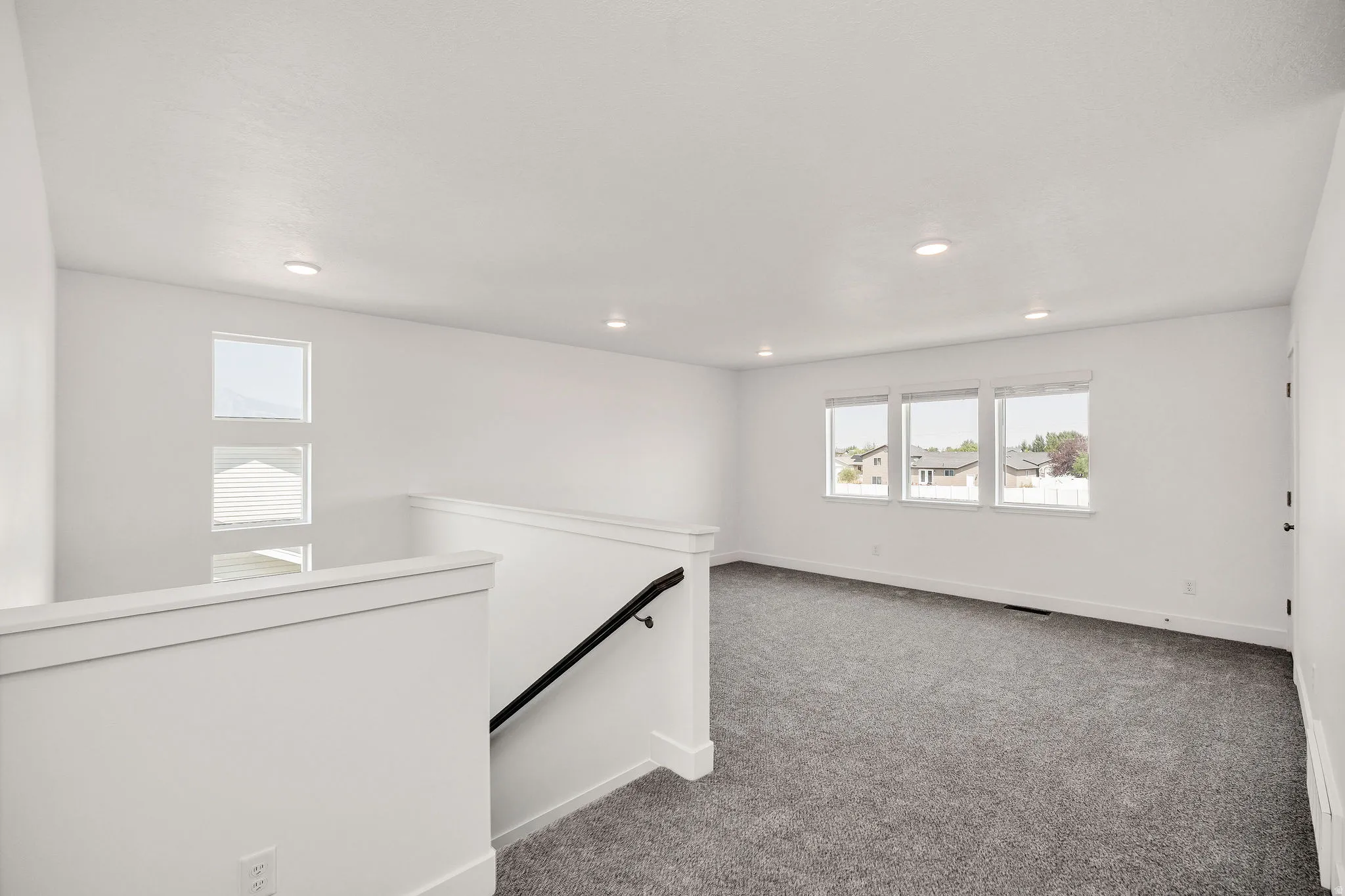 Bright upper-level space with recessed ceiling lighting, large multi-pane windows, neutral wall finishes with wainscoting detail, and gray carpet flooring