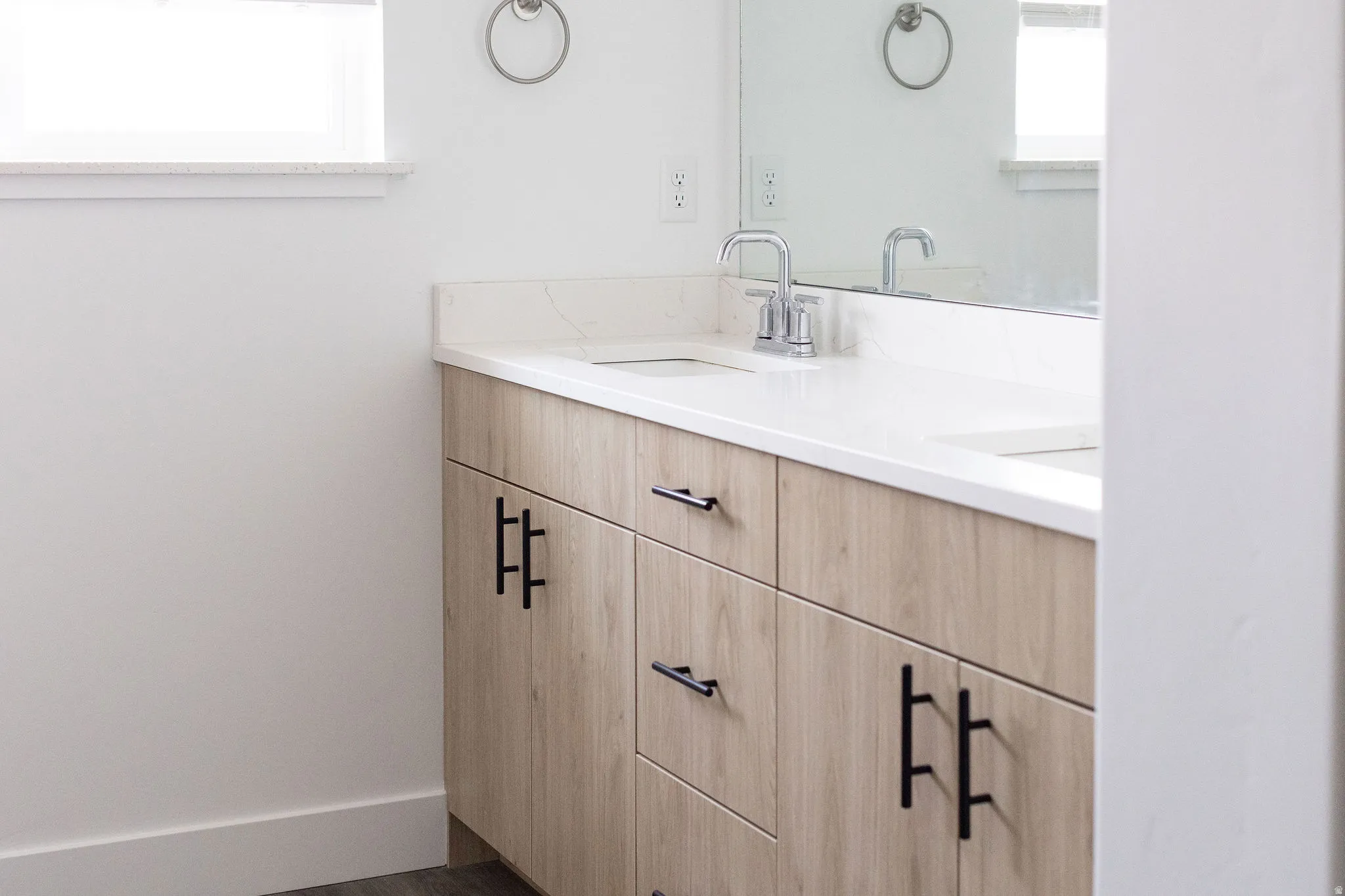 Modern bathroom vanity featuring a light wood-finish cabinet with chrome hardware, white quartz countertop, and a chrome faucet