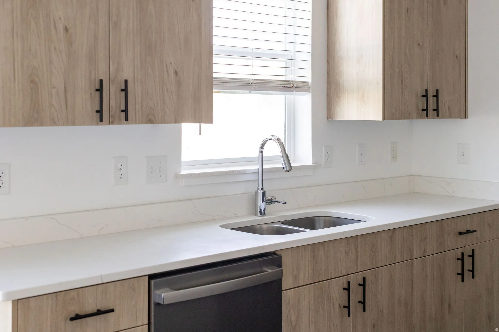 Wood-finish cabinetry with matte black hardware, white countertops, stainless steel double basin sink, and a stainless steel dishwasher