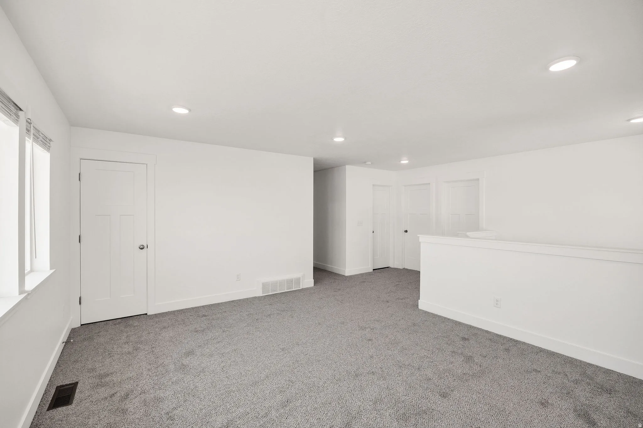Spacious open layout with neutral carpet flooring, recessed ceiling lighting, and multiple white six-panel doors