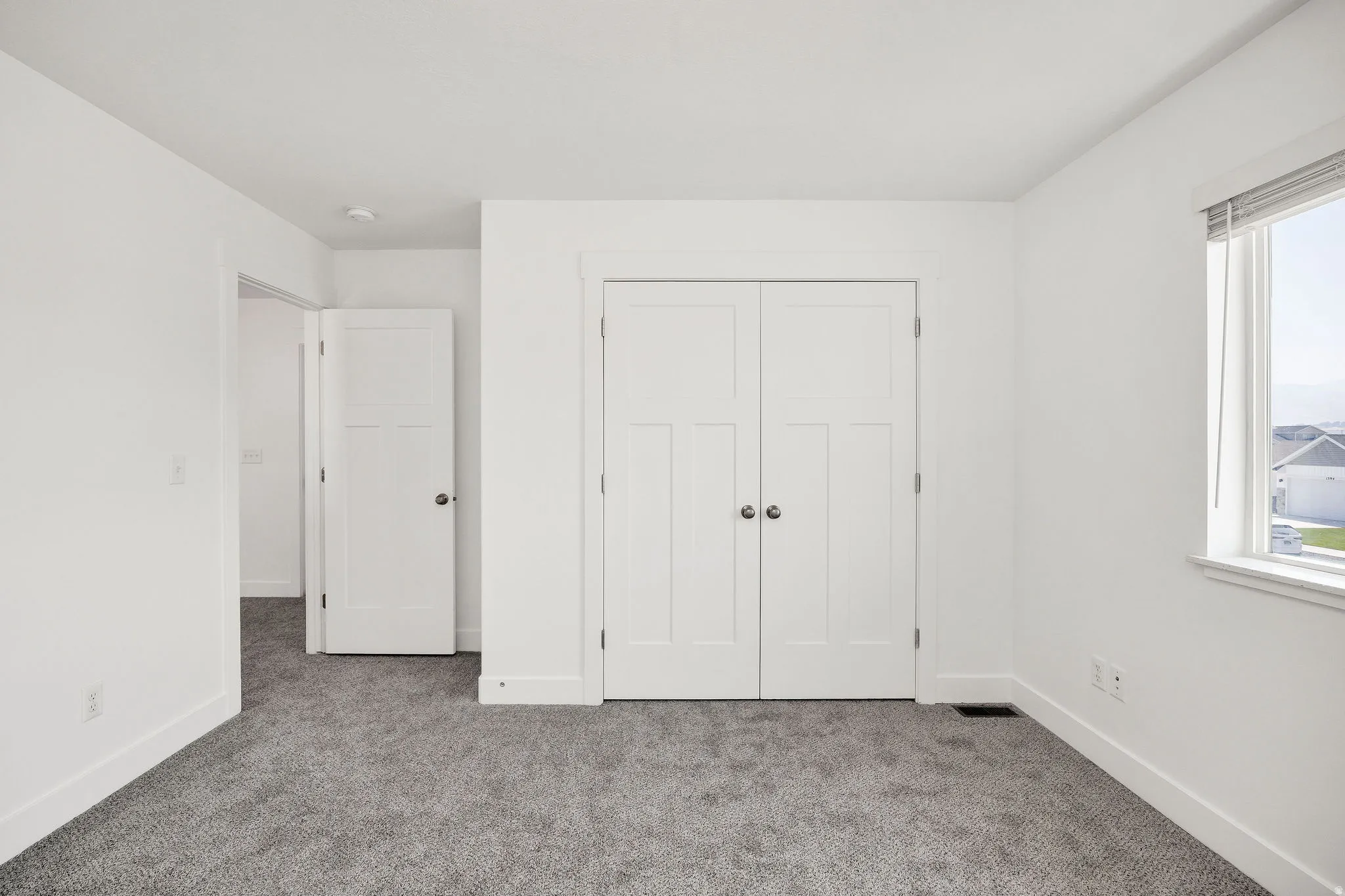 Neutral wall paint, gray carpeting, a window with blinds, and white interior doors