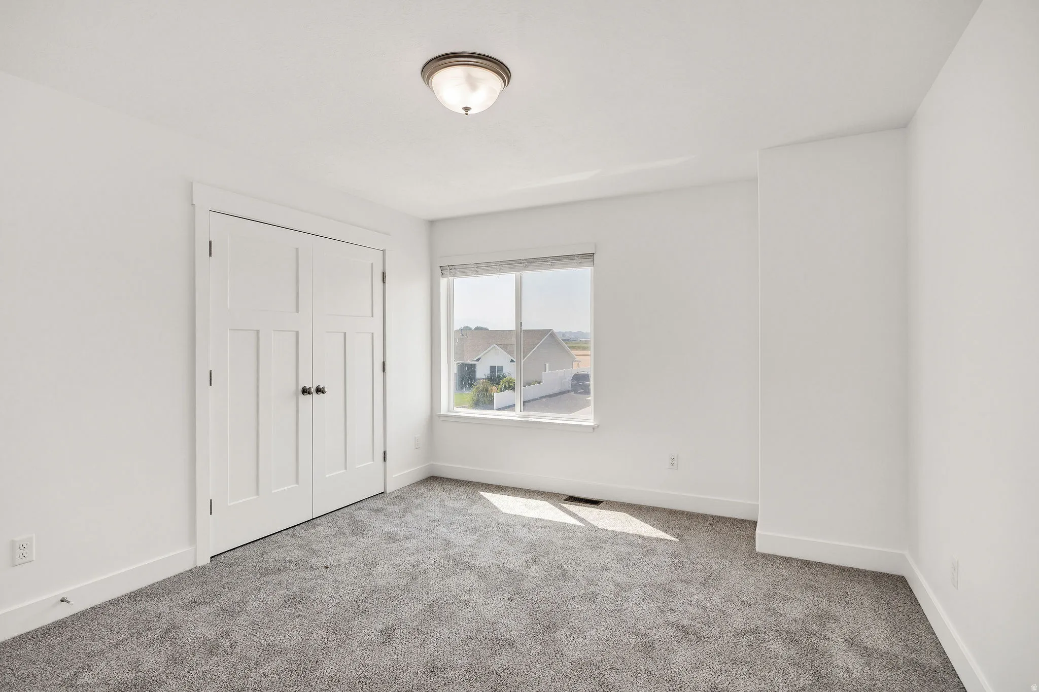 Carpeted interior with a window, white walls, and a flush-mount ceiling light