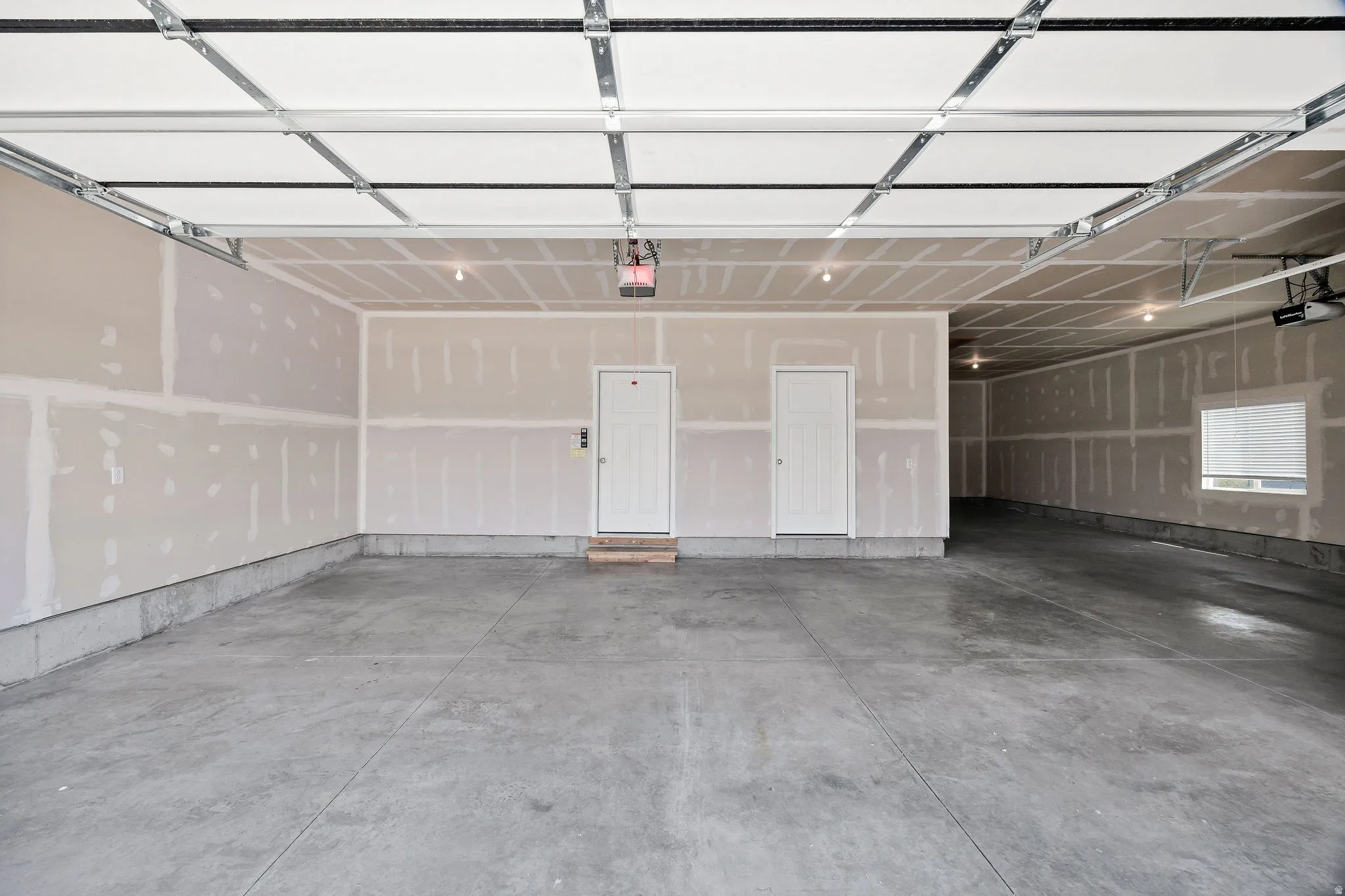 Spacious garage featuring polished concrete flooring, overhead sectional door with integrated opener, drywall-finished walls, and recessed lighting throughout