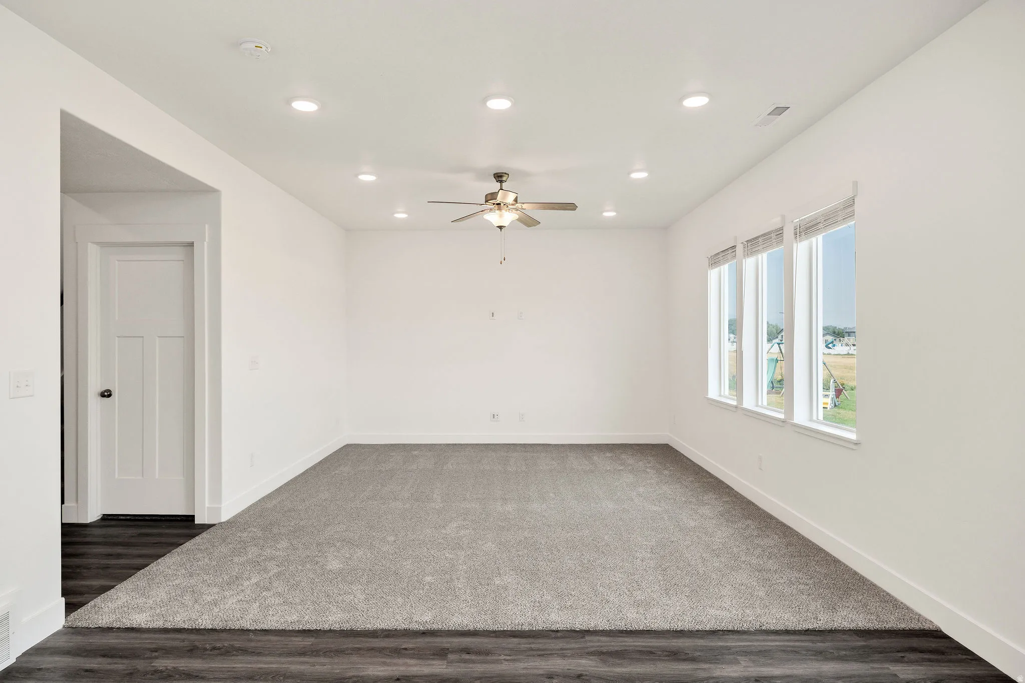 Recessed lighting, ceiling fan, multiple windows, light grey carpeting, and wood-finish flooring