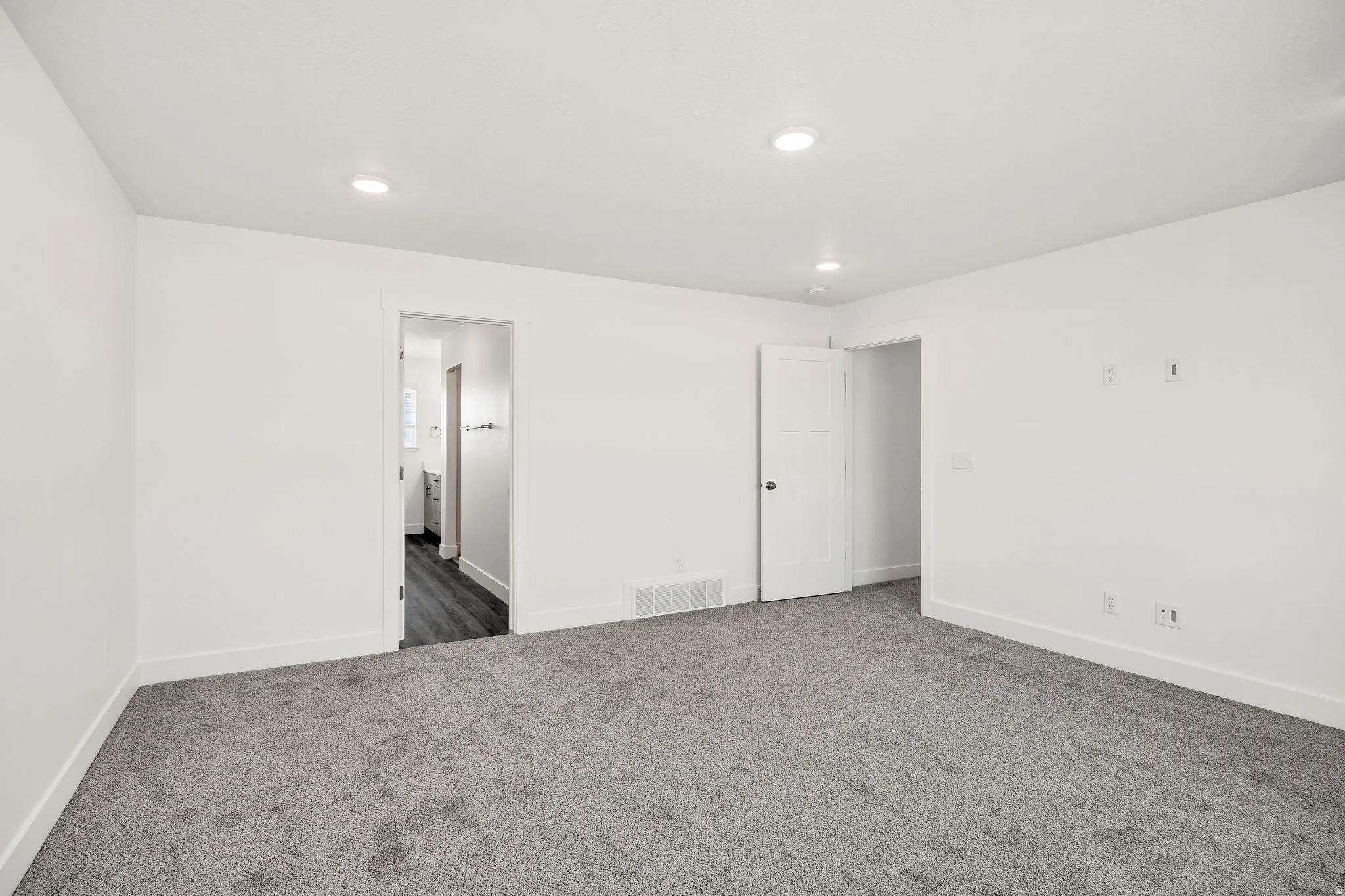 Spacious bedroom featuring neutral white walls, recessed ceiling lighting, and plush carpeting throughout