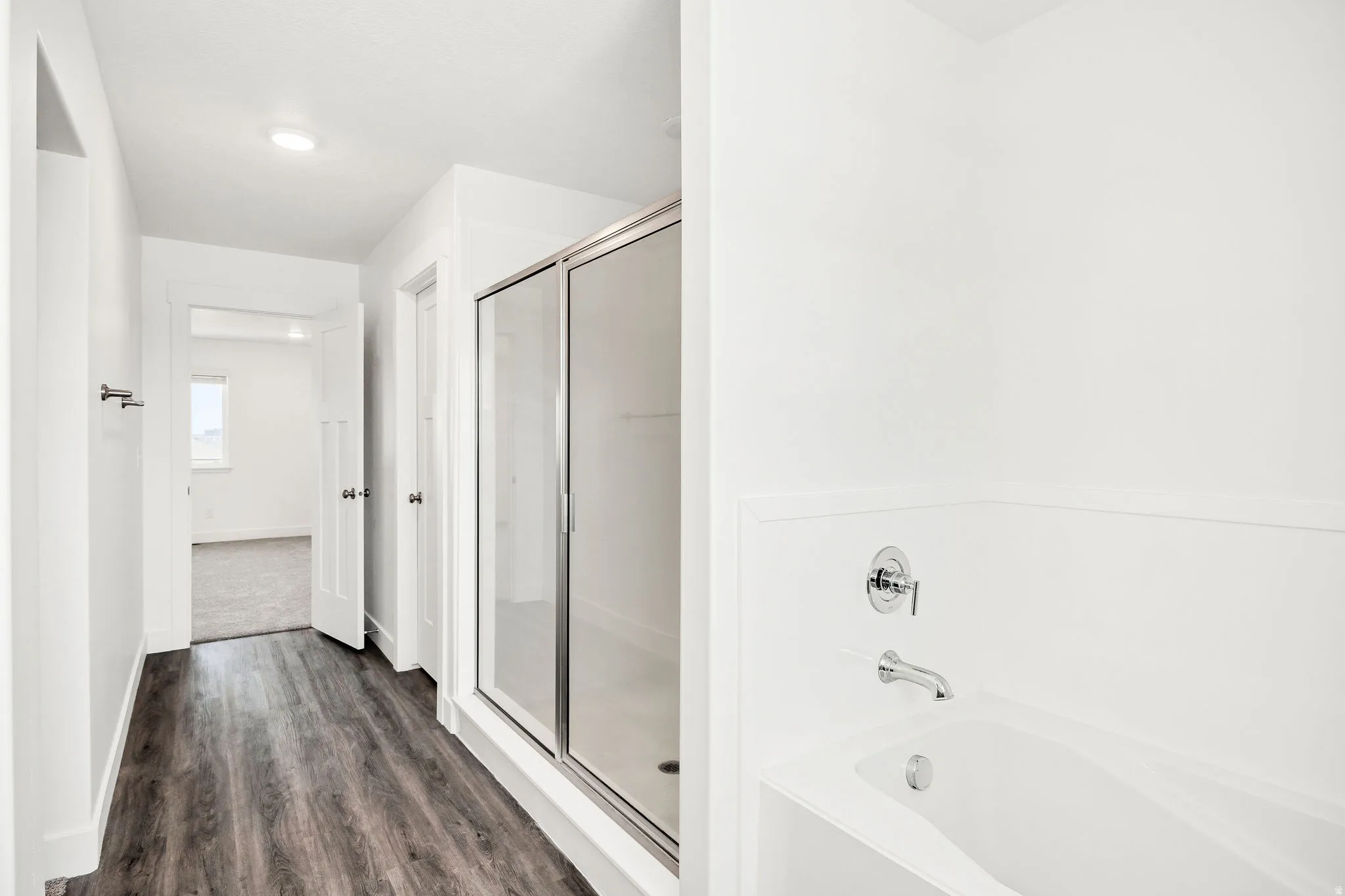 Primary bathroom featuring a soaking tub with chrome wall-mounted faucet and hand-held shower, framed by a large sliding glass enclosure