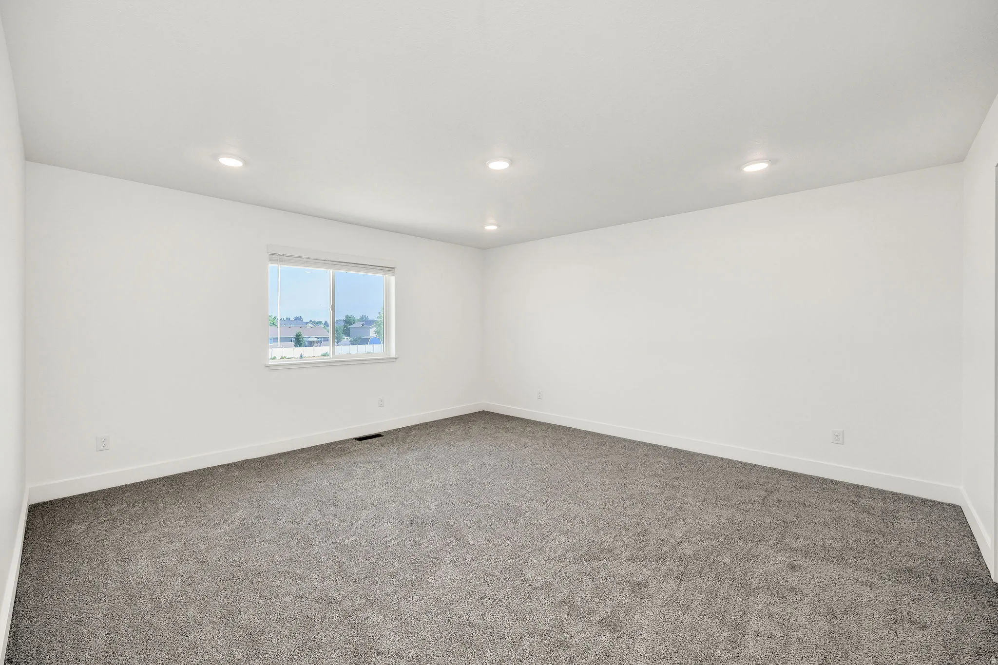 Spacious room featuring neutral white walls, recessed ceiling lighting, and soft gray carpet flooring