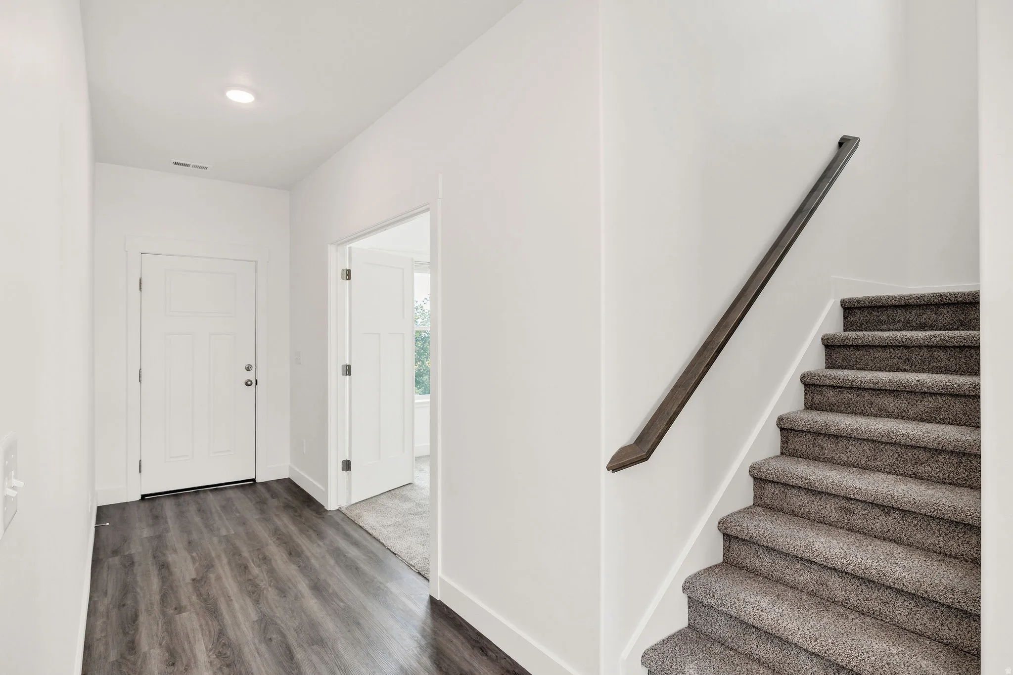 Wood-finish flooring, recessed ceiling lighting, a contemporary door with panel detailing, and a carpeted staircase with a dark handrail