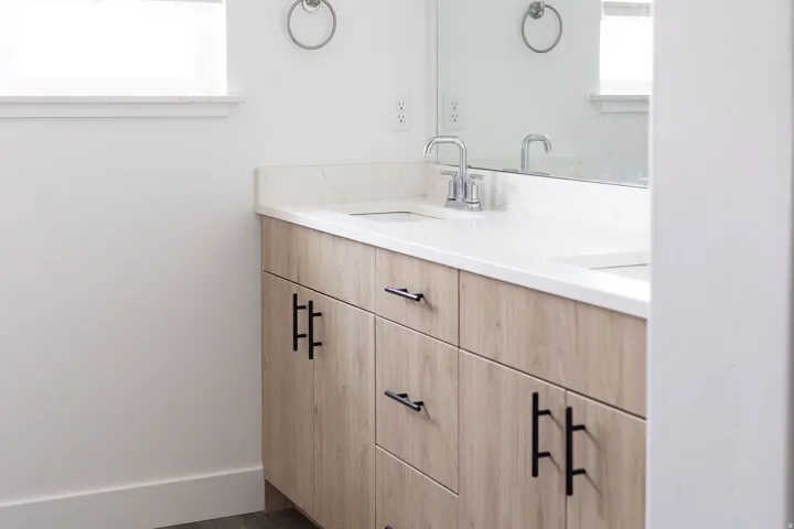 Modern bathroom vanity featuring a light wood-finish cabinet with chrome hardware, white quartz countertop, and a chrome faucet