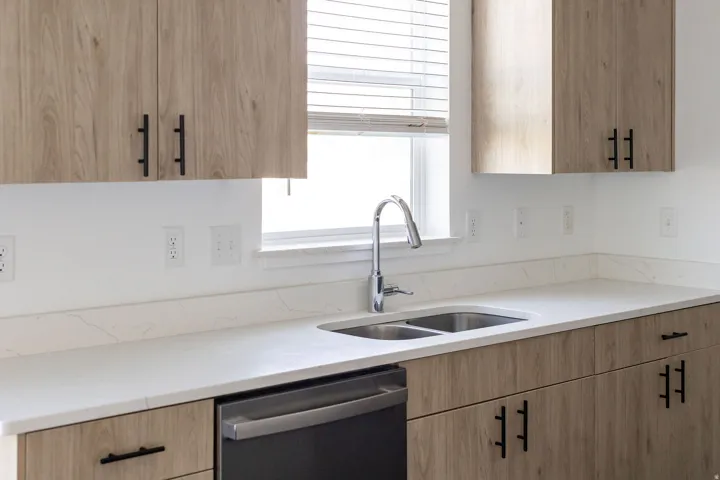 Wood-finish cabinetry with matte black hardware, white countertops, stainless steel double basin sink, and a stainless steel dishwasher