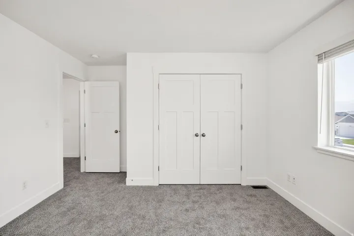 Neutral wall paint, gray carpeting, a window with blinds, and white interior doors