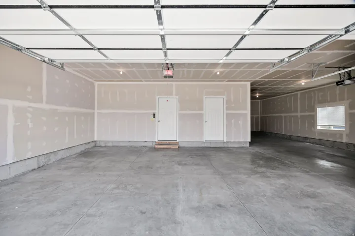 Spacious garage featuring polished concrete flooring, overhead sectional door with integrated opener, drywall-finished walls, and recessed lighting throughout