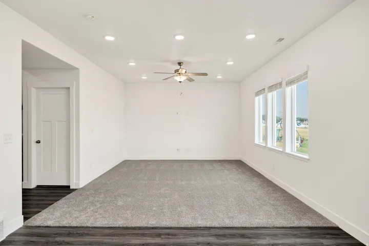 Recessed lighting, ceiling fan, multiple windows, light grey carpeting, and wood-finish flooring